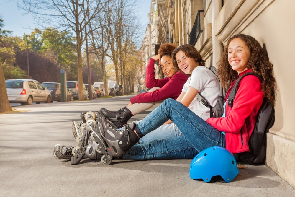Happy teens with rollerblades sitting at sidewalk